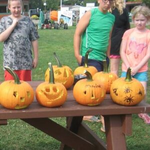 kids standing behind a picnic table covered with carved pumpkins